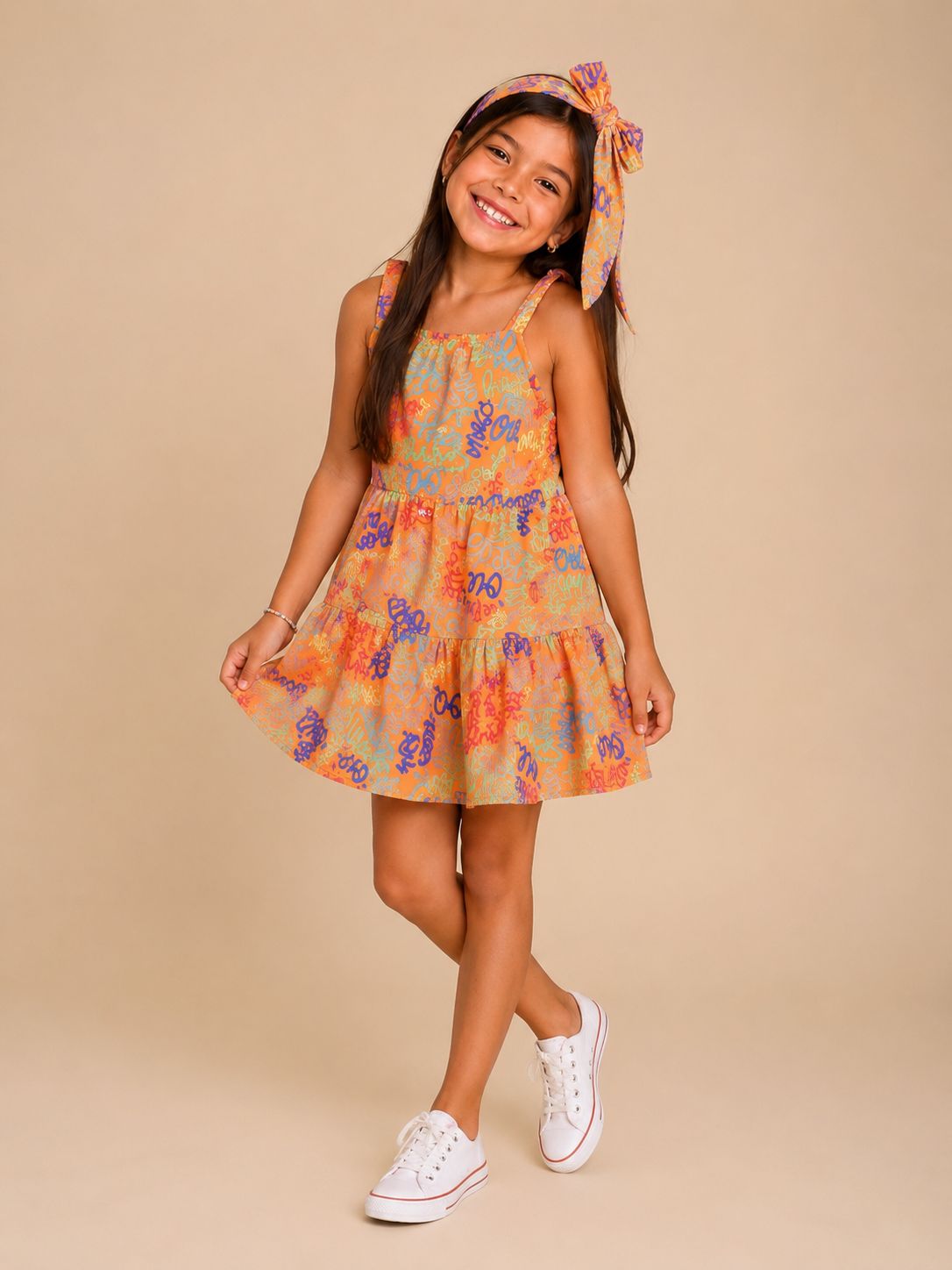Vestido infantil laranja com estampa de rabiscos coloridos e laço de cabelo combinando